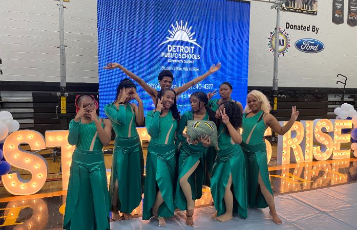 A group of eight Henry Ford High School dancers pose joyfully in matching emerald green